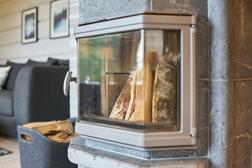 L&auml;hikuva huvilan modernista takasta, jossa polttopuut odottavat sytytt&auml;mist&auml;. Taustalla tunnelmallinen sisustus ja polttopuiden s&auml;ilytyskori.