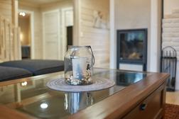 Eine stimmungsvolle Kerzenlaterne auf einem Glastisch im Wohnzimmer der Villa, mit einem modernen Kamin und hellen Holzpaneelen im Hintergrund.