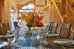 Ruokap&ouml;yt&auml; kauniisti katettuna syksyisell&auml; teemalla, kukka-asetelmia ja lasiastiat, taustalla huvilan l&auml;mminhenkinen sisustus ja puuportaikko.