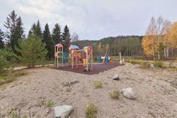Leikkipuisto Kolilla, jossa värikkäitä leikkitelineitä ja keinuja hiekkapohjaisella alueella, ympärillä metsä ja syksyinen luonto.