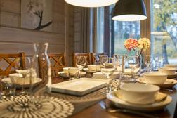 Ein elegant gedeckter Esstisch in der Villa, an dem Geschirr, Gläser und Blumenarrangements für eine gemütliche Atmosphäre sorgen. Große Fenster und Blick in die Natur im Hintergrund.