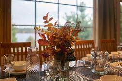 Syksyinen kukka-asetelma ruokap&ouml;yd&auml;ll&auml;, taustalla huvilan suuri ikkuna ja n&auml;kym&auml; j&auml;rvelle.