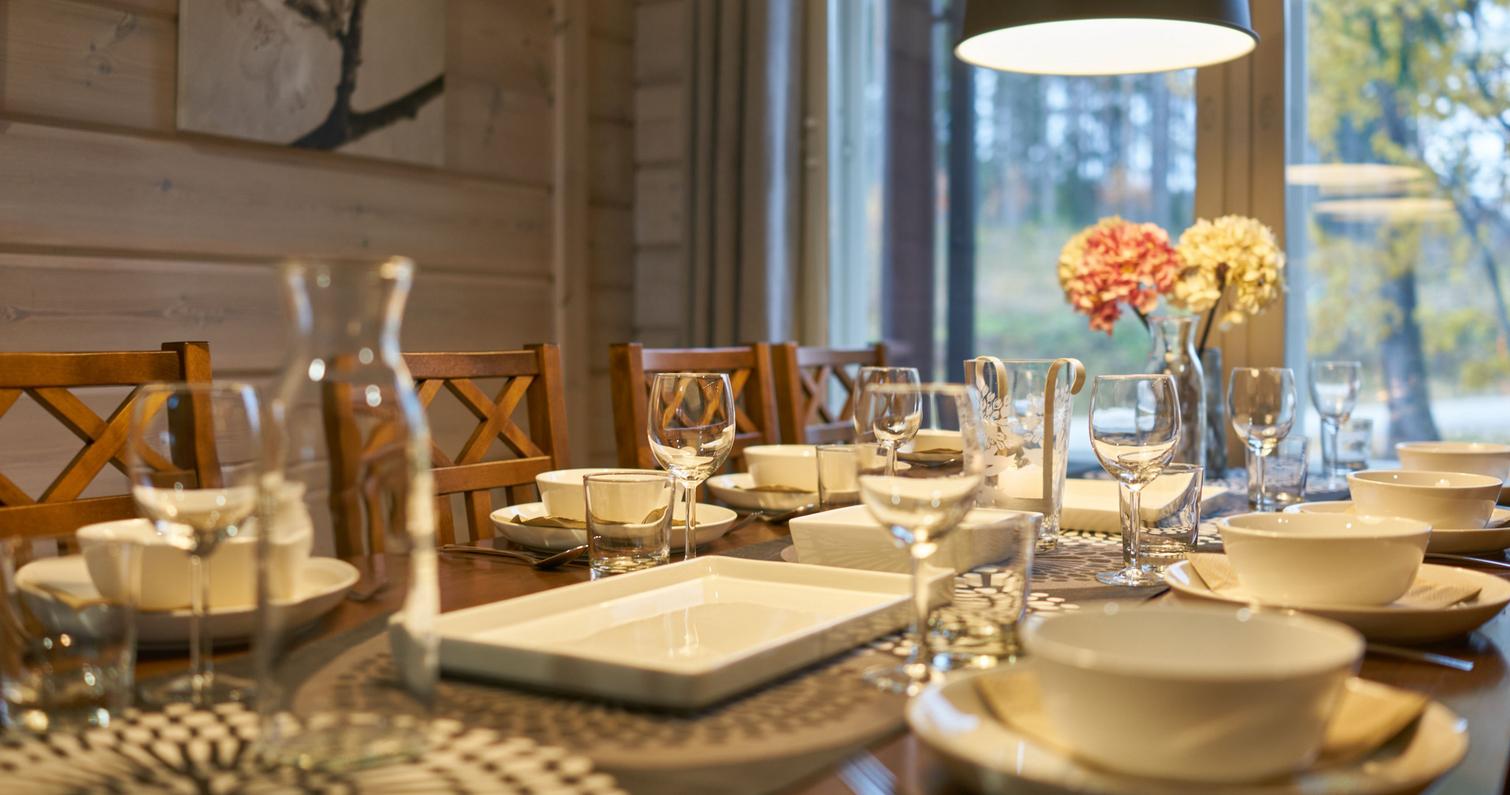 Ein elegant gedeckter Esstisch in der Villa, an dem Geschirr, Gläser und Blumenarrangements für eine gemütliche Atmosphäre sorgen. Große Fenster und Blick in die Natur im Hintergrund.