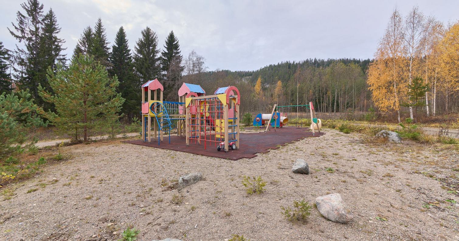 Leikkipuisto Kolilla, jossa värikkäitä leikkitelineitä ja keinuja hiekkapohjaisella alueella, ympärillä metsä ja syksyinen luonto.