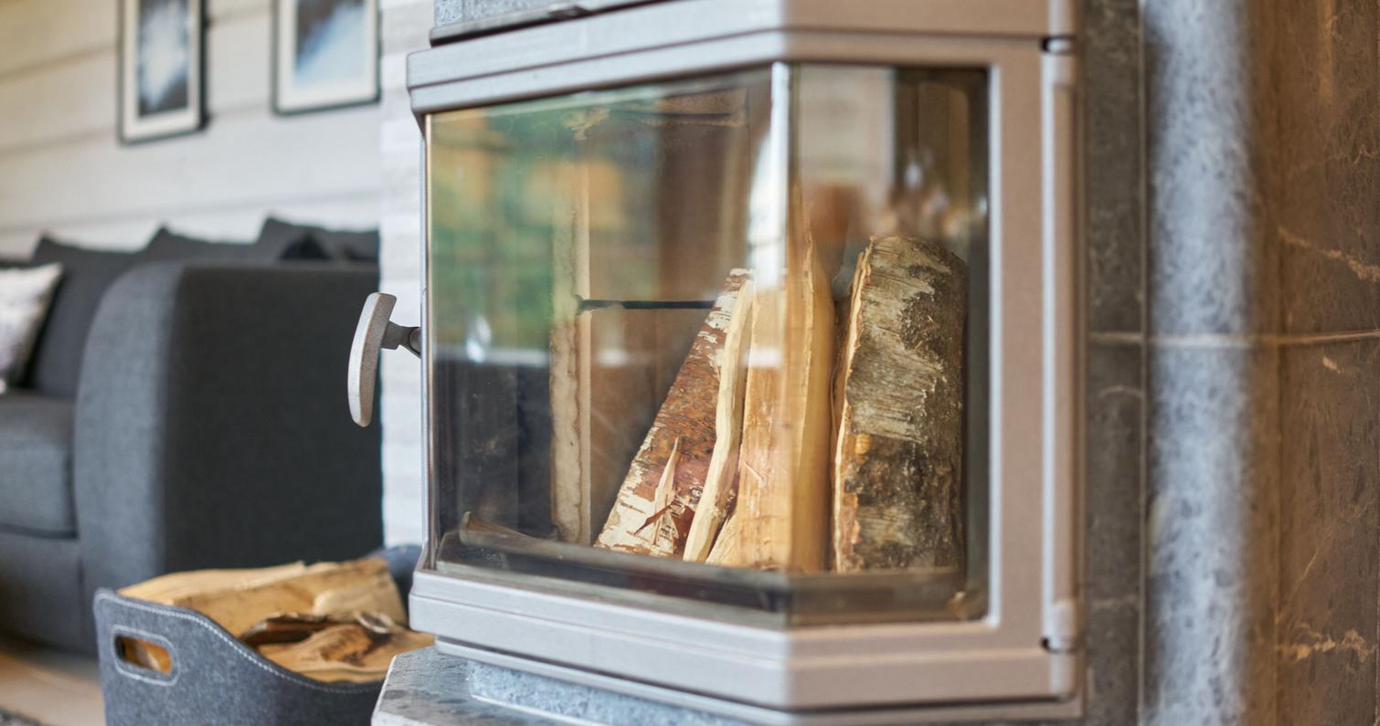 L&auml;hikuva huvilan modernista takasta, jossa polttopuut odottavat sytytt&auml;mist&auml;. Taustalla tunnelmallinen sisustus ja polttopuiden s&auml;ilytyskori.